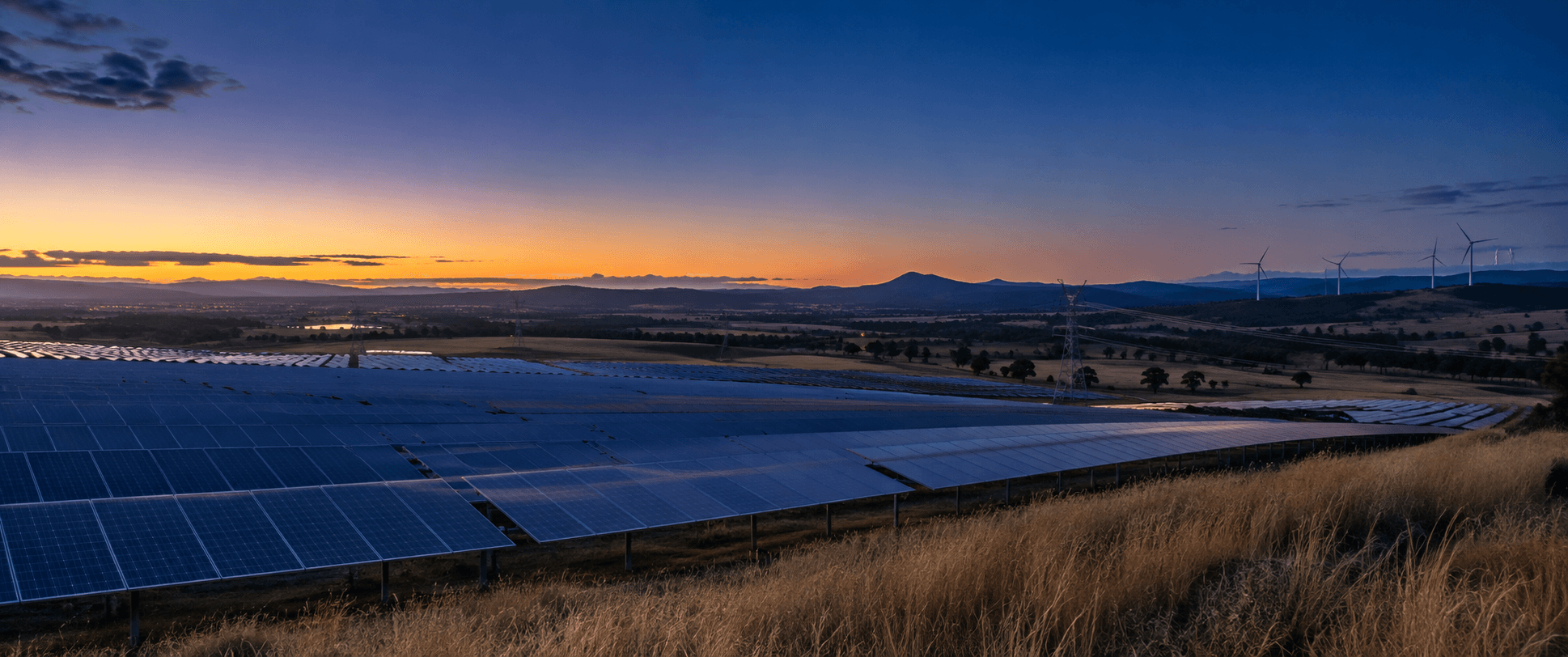 Solar fields, wind turbines and transmission lines across an open landscape at dusk